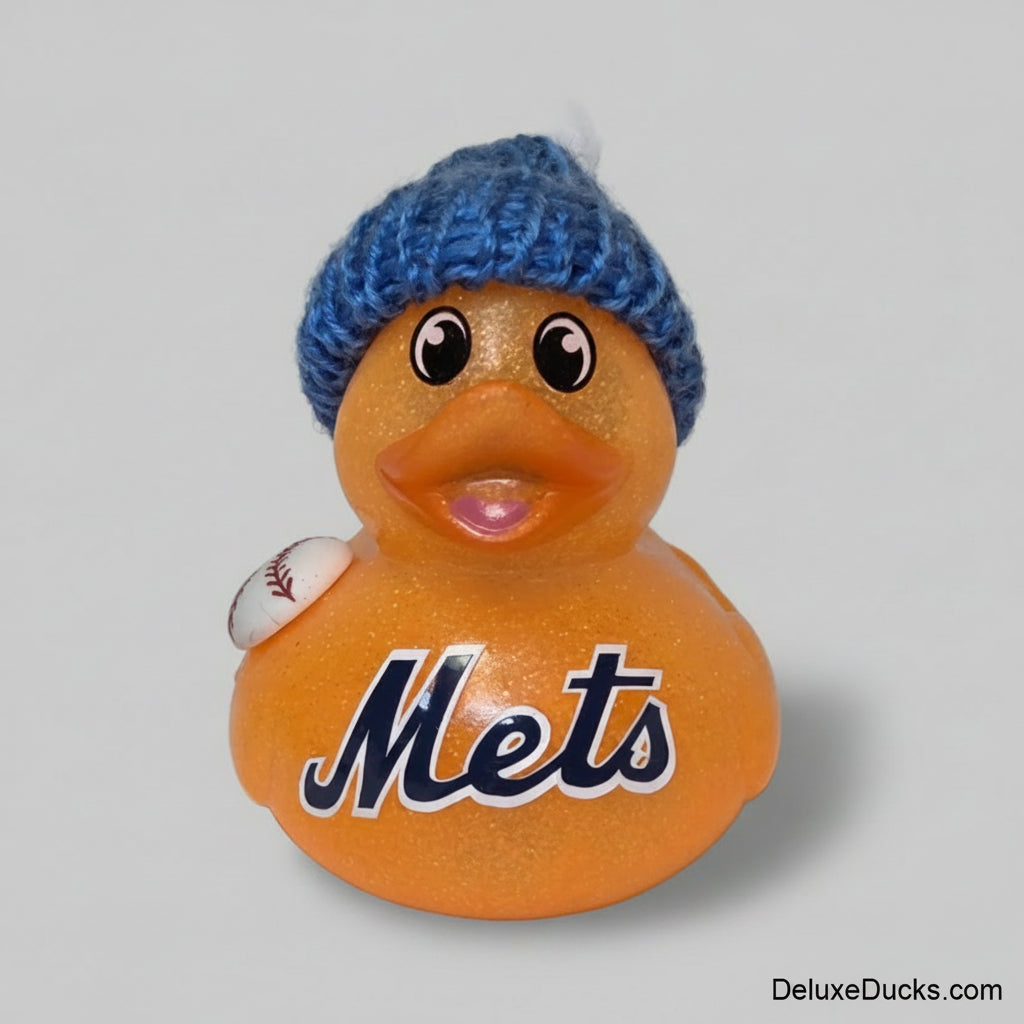 An orange glittery rubber duck with the word 'Mets' in navy blue script, wearing a blue knit beanie with a white pom-pom and holding a small baseball.