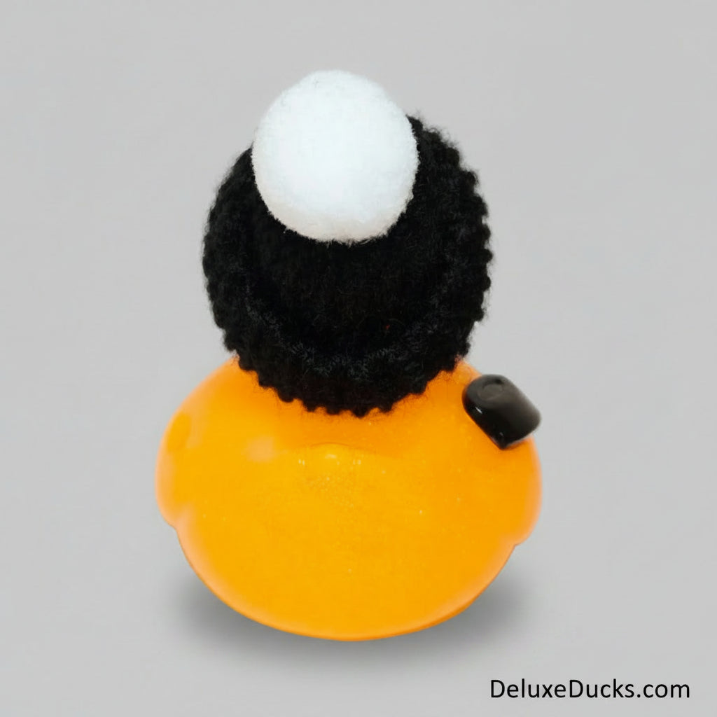 Small orange duck toy with a black hat and white ball on a light gray background