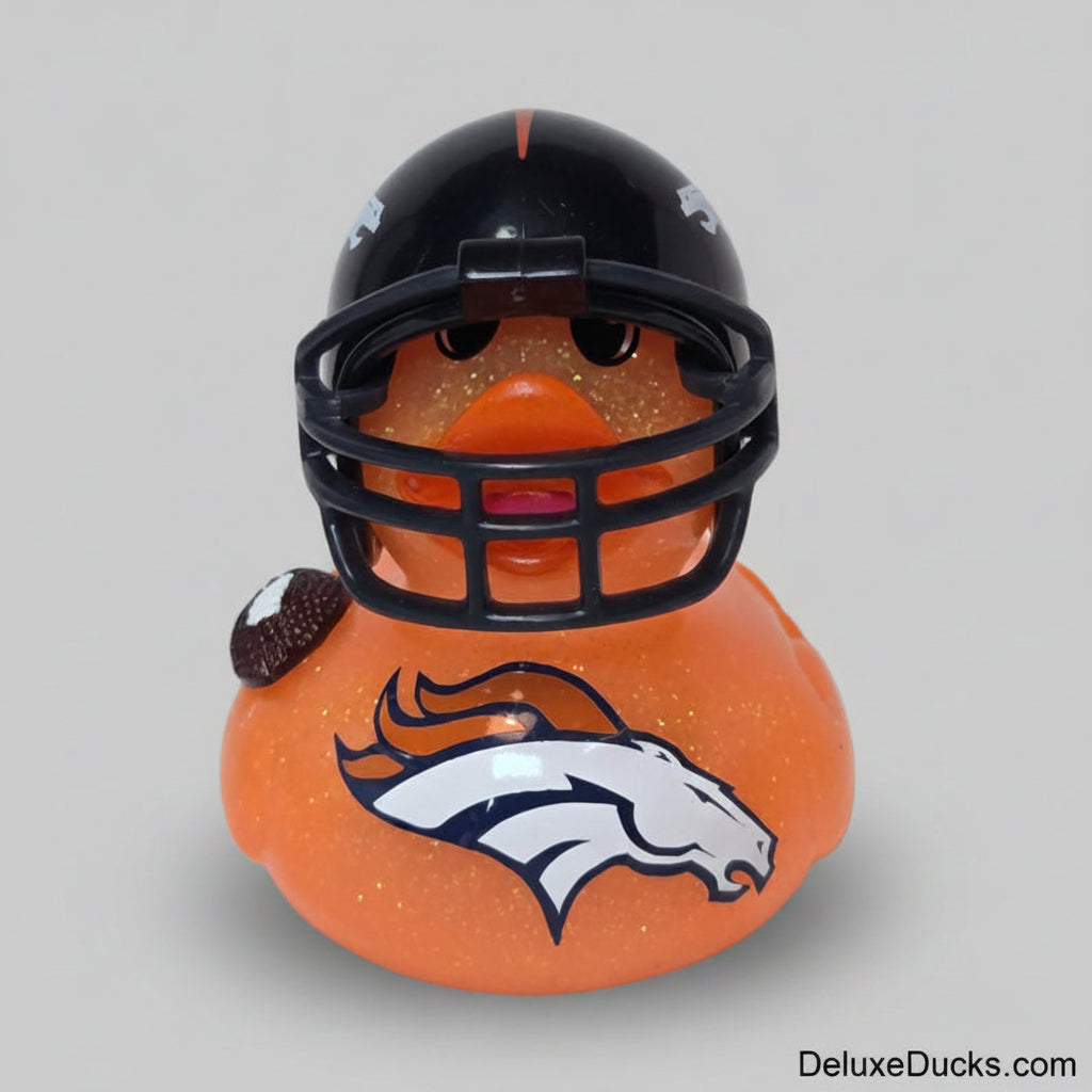 An orange glittery duck toy wearing a black football helmet with a faceguard and a small football accessory, featuring the Denver Broncos logo on the front, set against a plain light background.