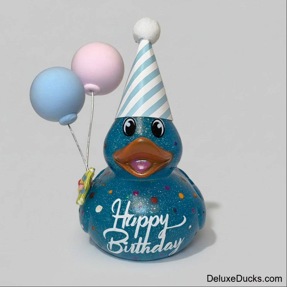 A blue glittery rubber duck decorated with colorful confetti, white 'Happy Birthday' script, a light blue and white striped party hat with a white pom-pom, and holding a blue and pink balloon.