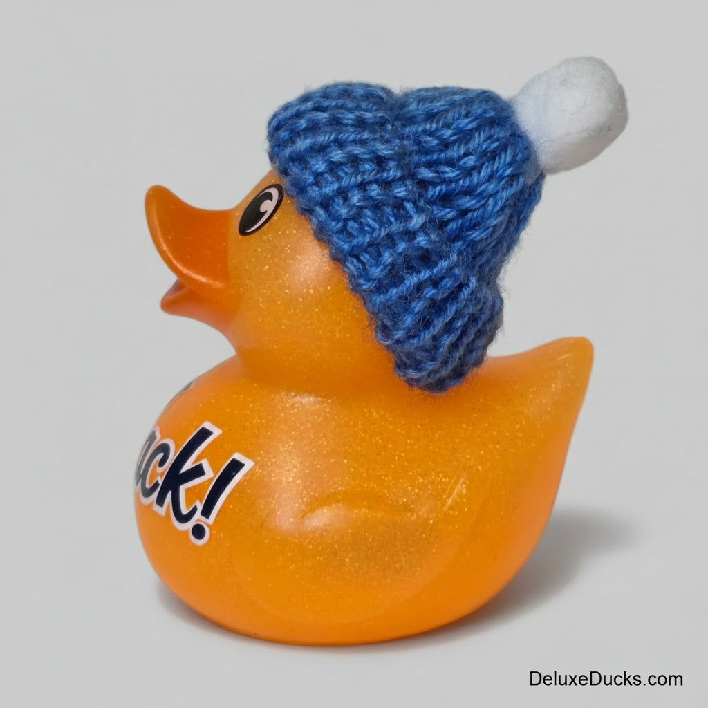 A glittery orange rubber duck wearing a blue knit beanie with a white pom-pom, photographed against a plain light background.