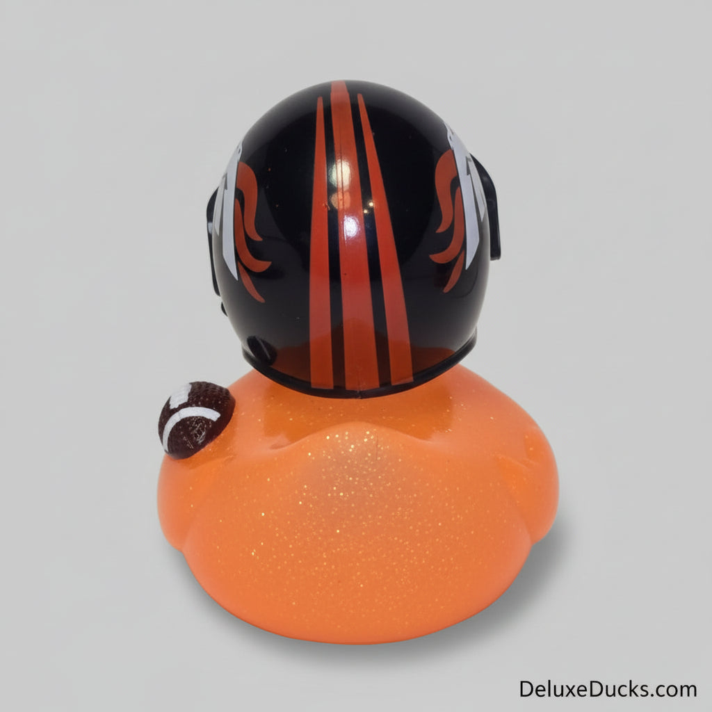 A novelty rubber duck with a glittery orange body and a black helmet with orange and white flame-like stripes, photographed on a plain light background.