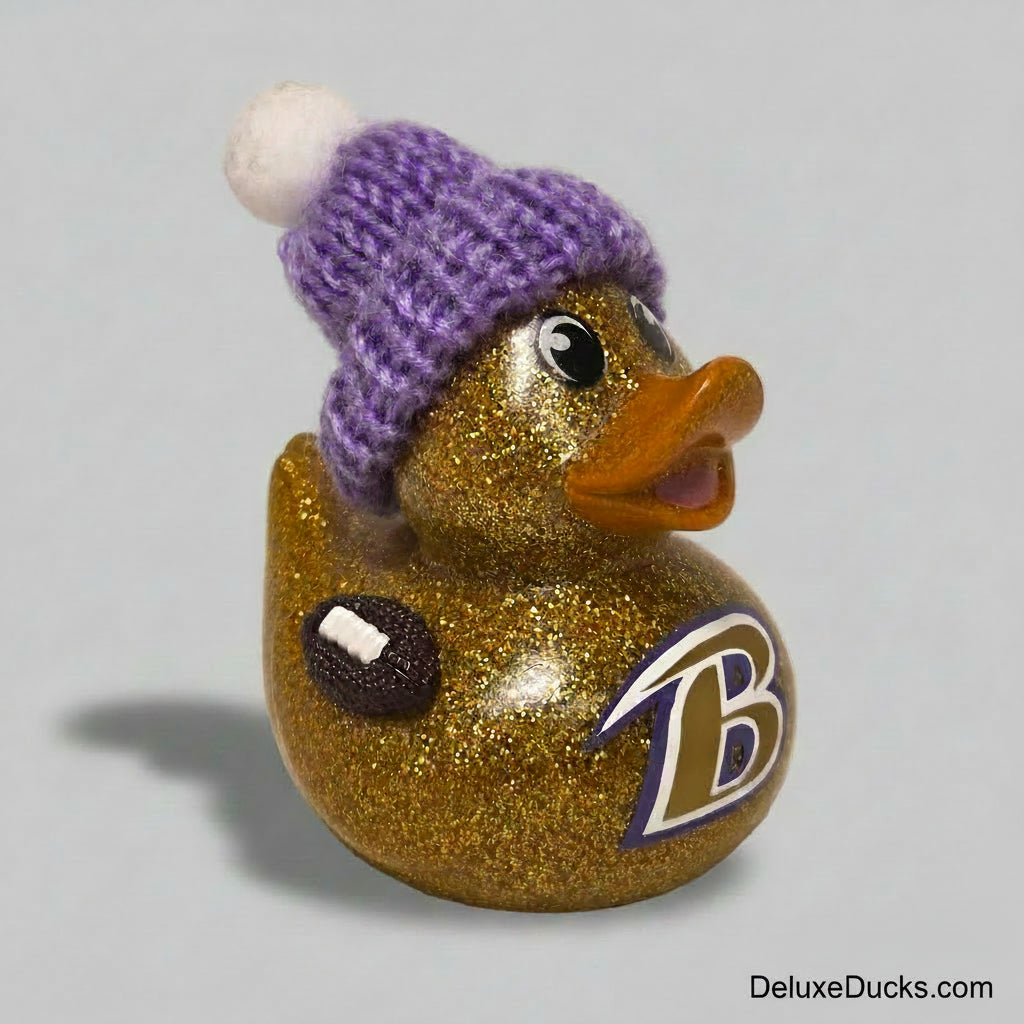 A glittery gold rubber duck with a purple knit beanie hat and a Baltimore Ravens logo, set against a plain light beige background.