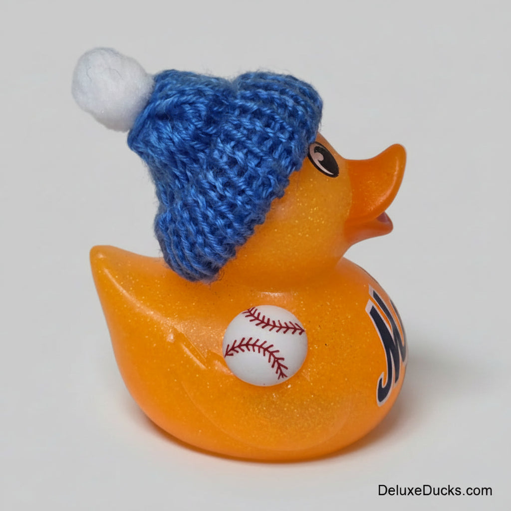 A glittery orange rubber duck with a blue knit beanie hat and white pom-pom, featuring a baseball decal on its side.